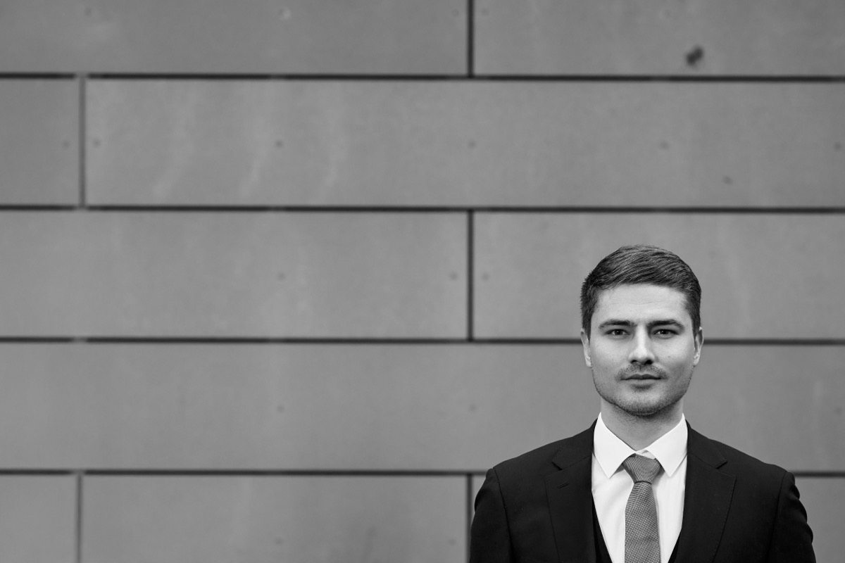 Marcel Wörner im Anzug vor einer Wand aus Betonplatten, schwarz-weiß